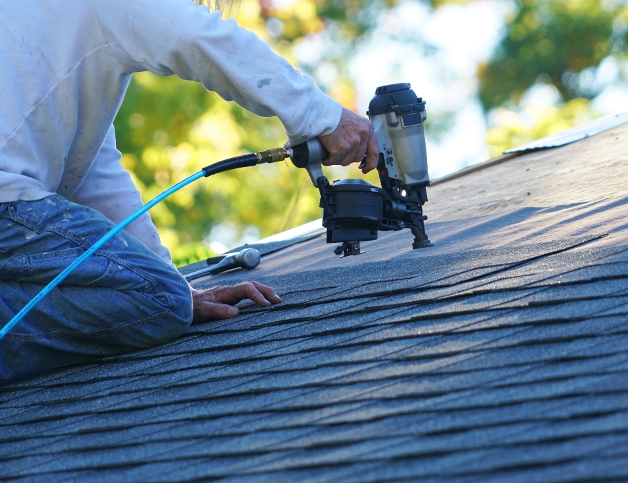 A West Orange Roofing crew member using a nail gun to secure asphalt shingles on a roof.