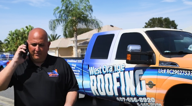 A West Orange Roofing team member standing next to a company vehicle talking on the phone