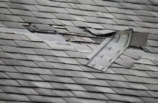 Damaged asphalt shingle roof with lifted and missing shingles, showing need for professional roof repair — expert roofing services and storm damage repair available near you.